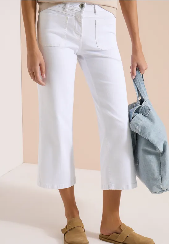 Witte, licht uitlopende cropped jeans met sandalen en denim schoudertas.