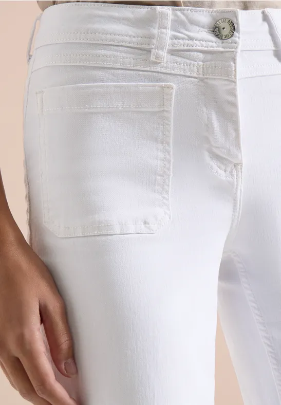 Close-up van een witte, nauwsluitende jeans met voorzak en hand op het bovenbeen.