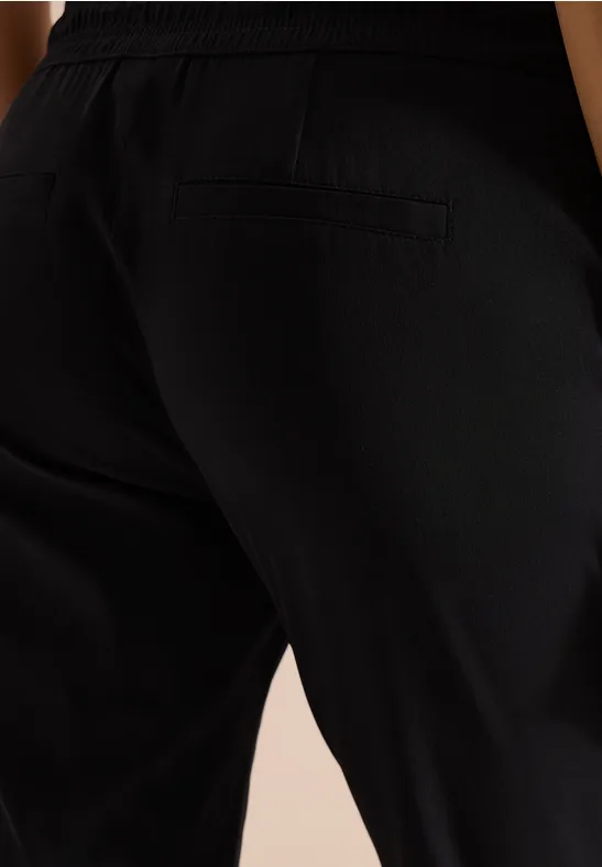 Close-up van een persoon in zwarte broek, zijdelingse heup- en beenpartij met zak.