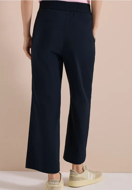 Vrouw van achteren in een donkerblauwe, wijde broek met elastische taille, gecombineerd met beige sneakers.