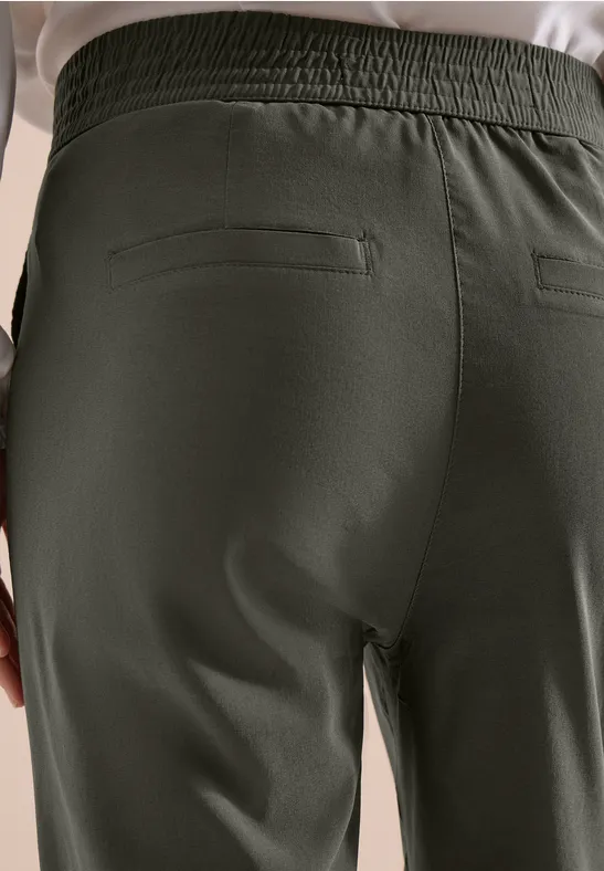 Rugaanzicht van donkergroene broek met elastische tailleband en achterzak met rits.