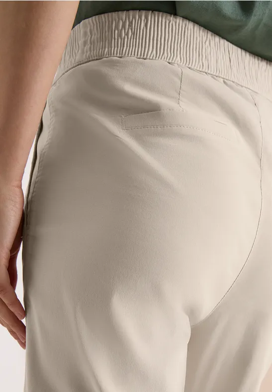 Close-up van een persoon in beige, hoog getailleerde broek met elastische tailleband.