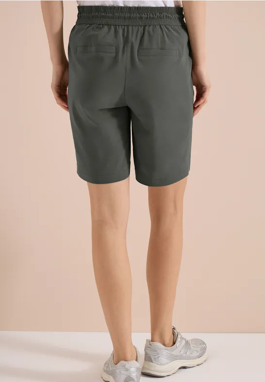 Achteraanzicht van iemand in knielange kaki short met witte sportschoenen