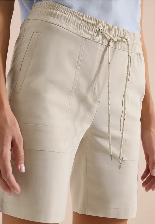 Crèmekleurige bermudashorts met elastische taille en koord, gecombineerd met een lichtblauw shirt.