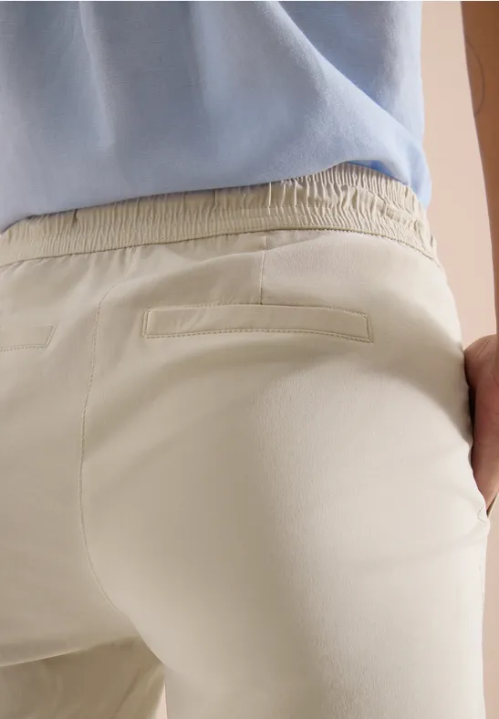 Achteraanzicht van een persoon in lichtbeige broek en blauw shirt, met de rechterhand in de achterzak.