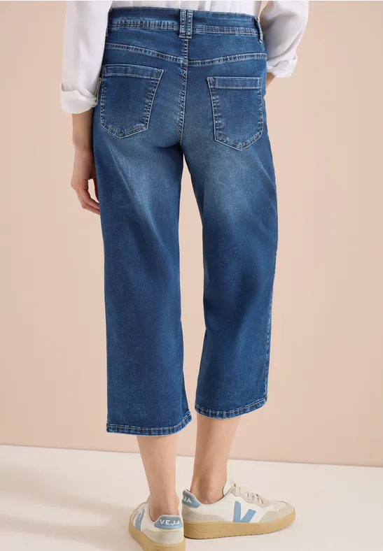 Rückansicht einer Person in weiten, knöchellangen Jeans-Culottes und weißen Sneakern.