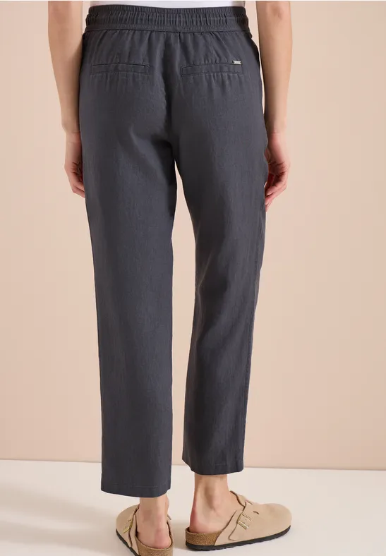 Rückansicht einer Person in grauen, locker sitzenden Hosen und beigen Slippern.