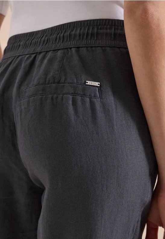 Hinterer Teil einer Person in dunkelgrauen Leinenhosen mit Gummibund und aufgesetzter Tasche samt kleinem Metalllogo