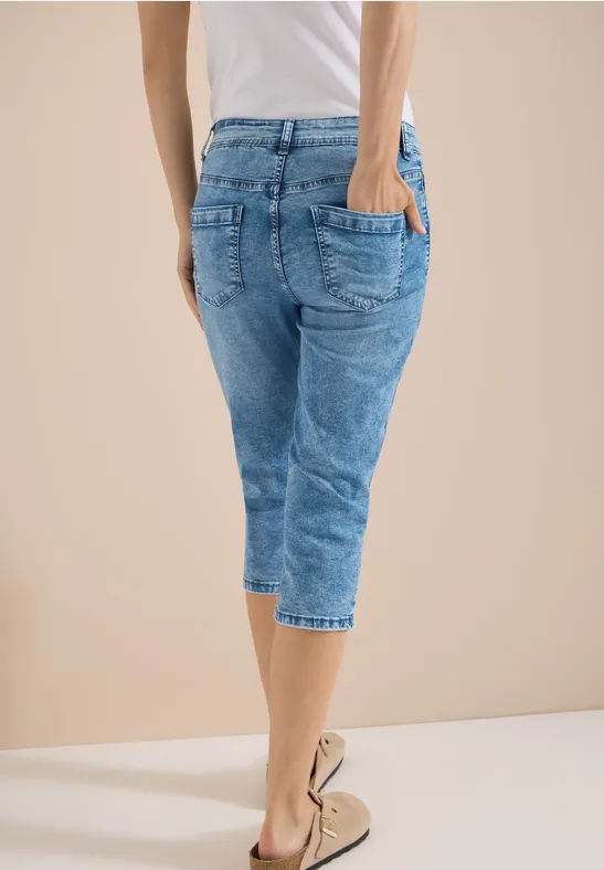 Person von hinten in hellblauer Capri-Jeans und beigen Espadrilles vor hellem Hintergrund.