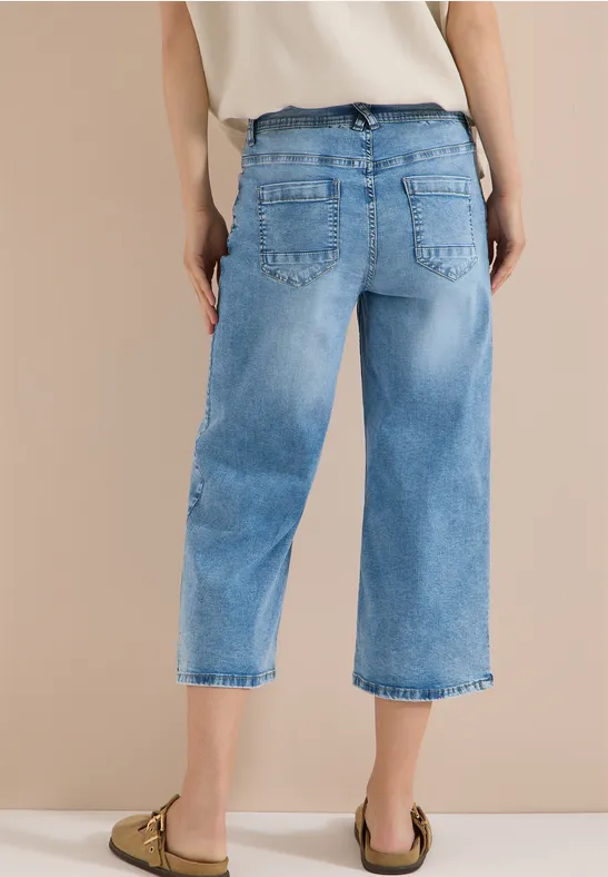 Hintenansicht einer Person in hellblauen, weiten 3/4-Jeans und beigen Slippern.