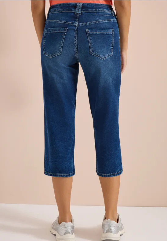 Person trägt blaue Capri-Jeans und weiße Turnschuhe.