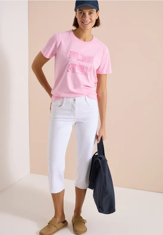 Vrouw in roze T-shirt, witte cropped jeans, bruine loafers en donkerblauwe tas.