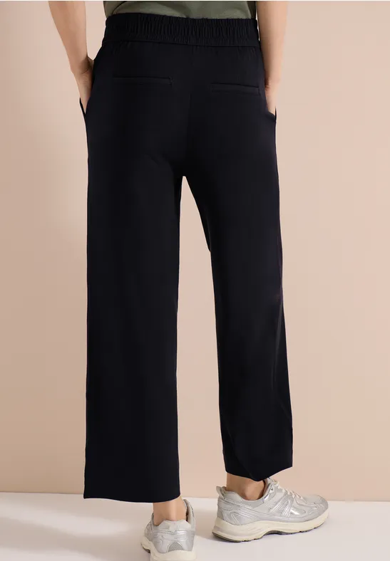 Schwarze, gerade geschnittene Hose mit aufgesetzten Taschen und elastischem Bund, kombiniert mit sportlichen Sneakern.