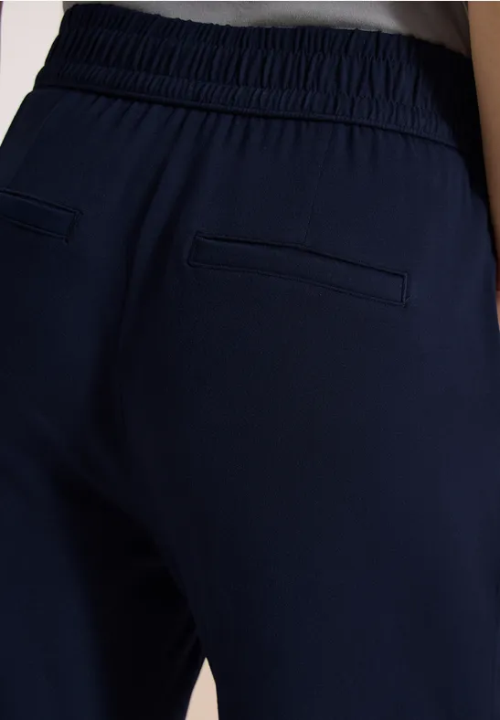 Rückansicht einer Person in dunkelblauen Hosen mit elastischem Bund und zwei Gesäßtaschen.