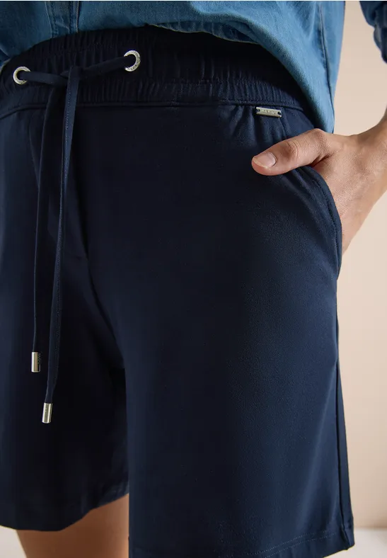 Nahaufnahme einer Person in dunkelblauen Jersey-Shorts mit Kordelzug und seitlicher Tasche.