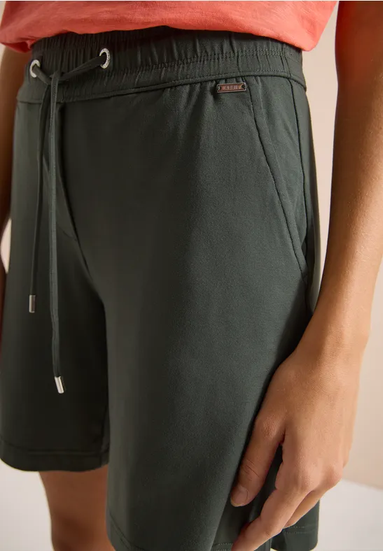 Nahaufnahme einer dunkelgrünen Shorts mit Kordelzug und Hand am Oberschenkel.