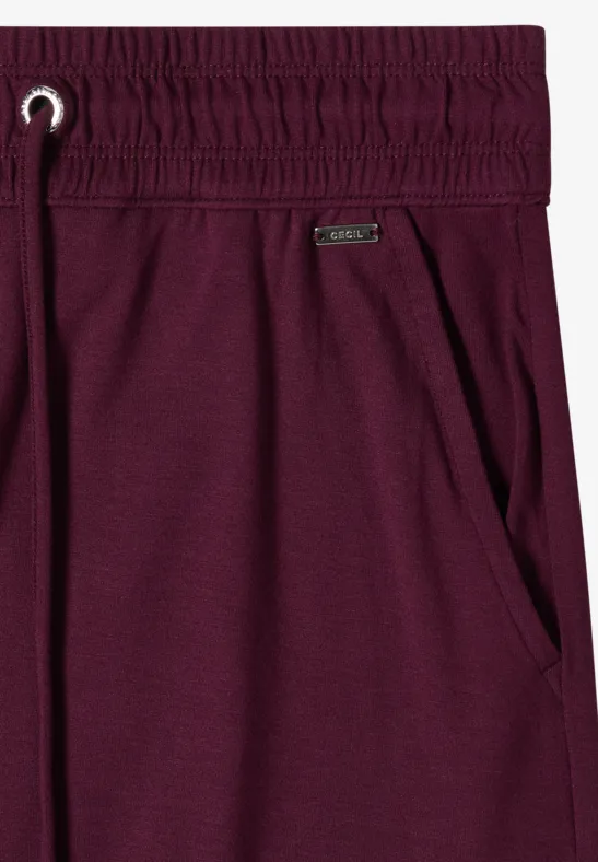 Lila Freizeithose mit elastischem Bund, Tunnelzug, seitlicher Tasche und Metall-Logo.
