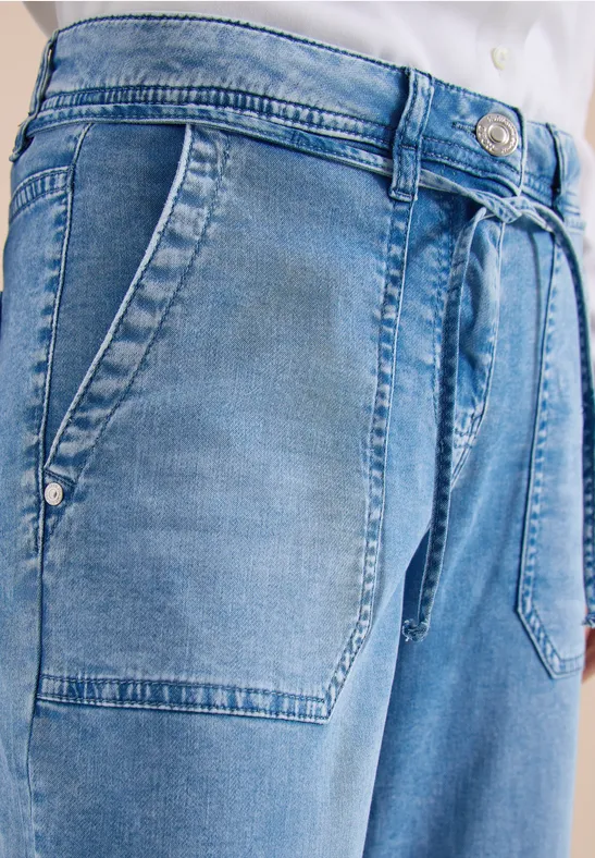 Blaue Jeanshose mit aufgesetzten Taschen und Stoffgürtel vorne, lässiger Schnitt.