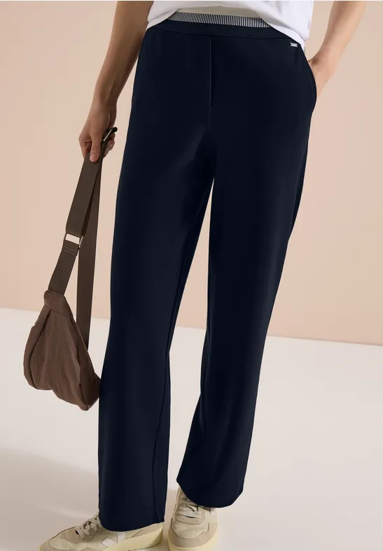 Pantalon large bleu foncé, baskets blanches et sac marron en style décontracté.