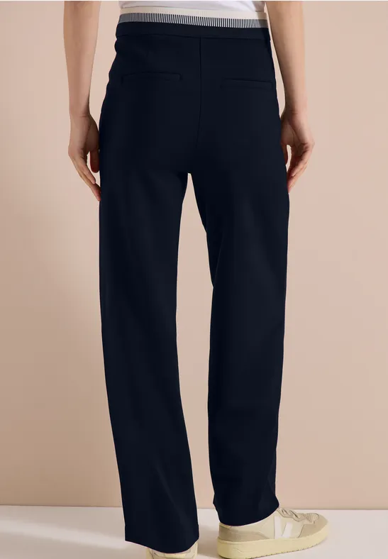 Personne de dos en pantalon noir ample et baskets blanches.