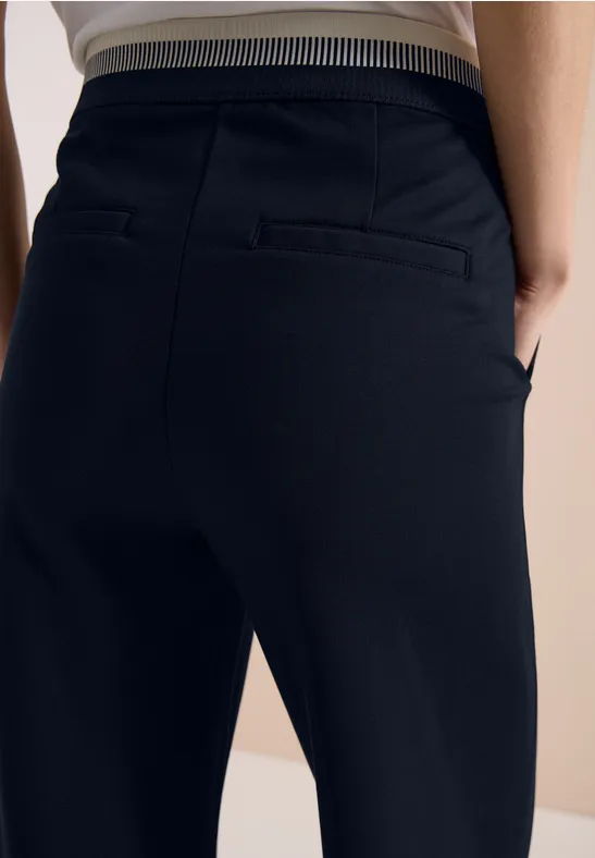 Personne vue de dos portant un pantalon noir ajusté avec taille élastique rayée.