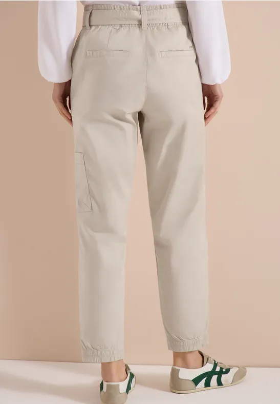 Beige Geradehose mit hohem Bund und elastischem Abschluss, dazu weiße Sneaker mit grünen Details.