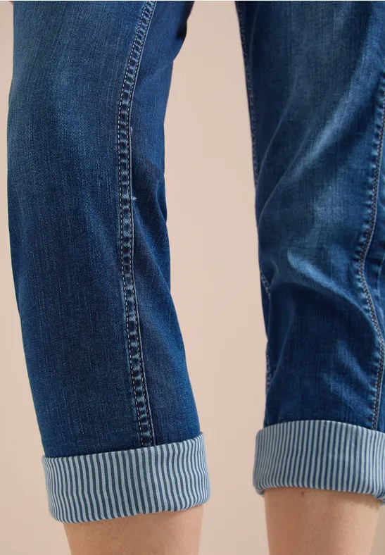 Blaue Jeansbeine mit umgeschlagenem Saum vor neutralem Hintergrund.