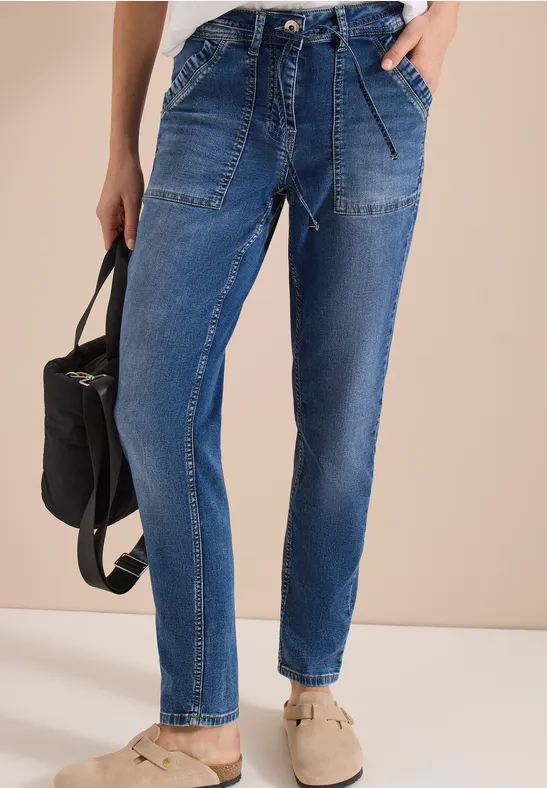 Blaue Jeans mit aufgesetzten Taschen und Gummizugbund, bequeme Schuhe und einen schwarzen Rucksack.