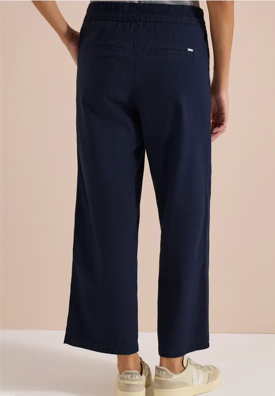 Achteraanzicht van persoon in wijde marineblauwe broek tot net boven de enkels met lichte sneakers.