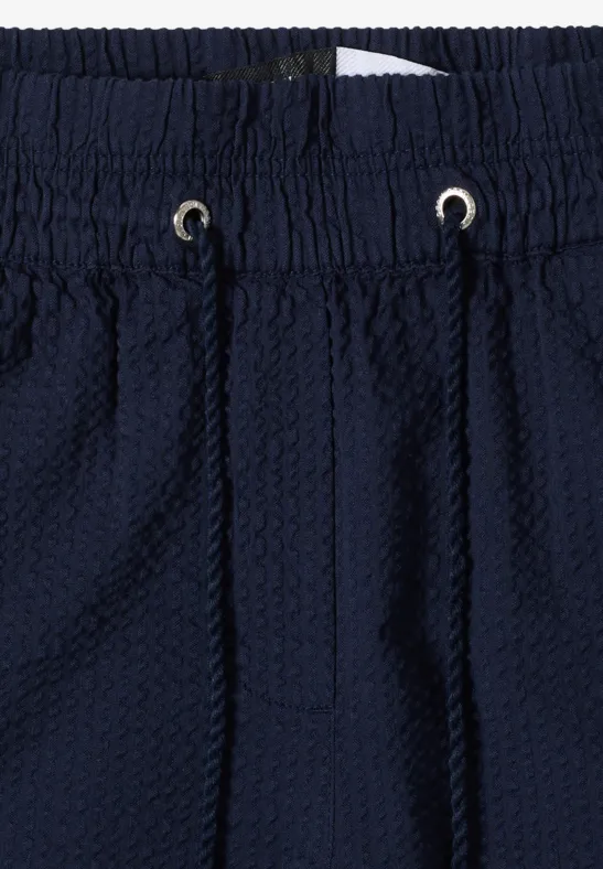 Close-up van een donkerblauwe, gestructureerde broek met elastische tailleband en aantrekkoord.