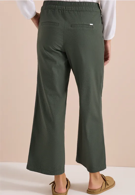 Achteraanzicht: model draagt donkergroene, wijde enkelbroek met elastische taille en casual loafers.