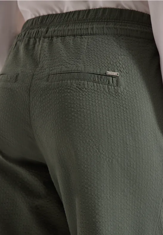 Achteraanzicht van een persoon in een gestructureerde olijfgroene broek met ritszak.