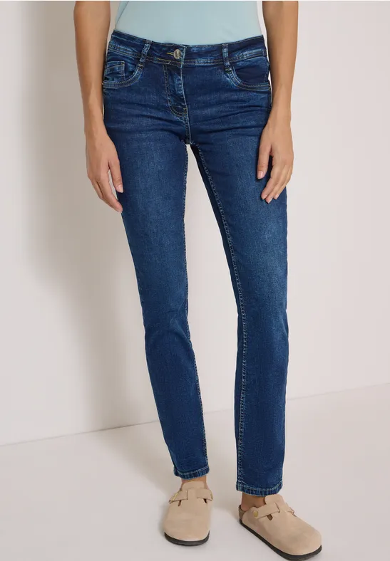 Jean bleu foncé pour femme, coupe ajustée, porté avec des mocassins beiges.