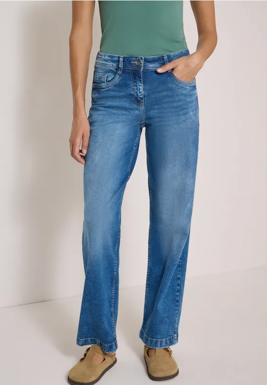 Stehende Person mit hellblauer, gerader Jeans im Used-Look und beigefarbenen Wildleder-Slippern.