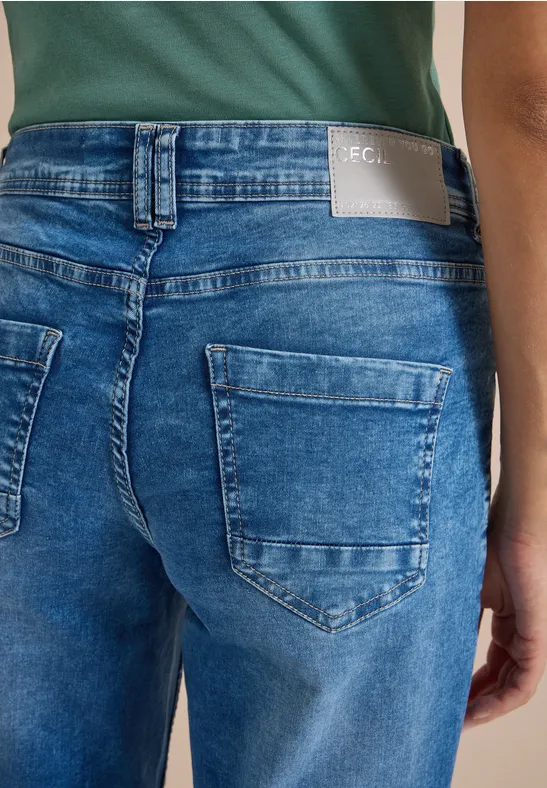 Rückansicht einer Person in blauen Jeans mit aufgesetzten Taschen und grünem Oberteil.
