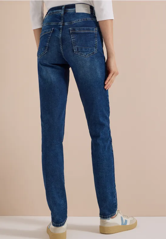 Frau von hinten in dunklen Jeans, weißem Gürtel und Sneakern.