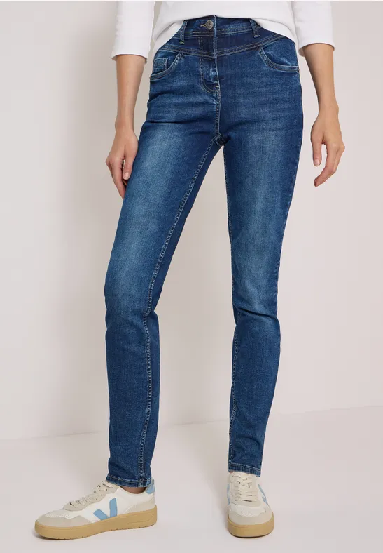 Person trägt blaue Skinny Jeans und weiße Sneakers, minimalistischer Hintergrund.