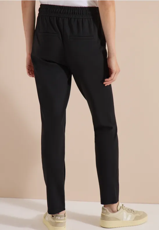 Schwarze Hose mit schmalem Schnitt und elastischem Bund, kombiniert mit beigen Sneakers.