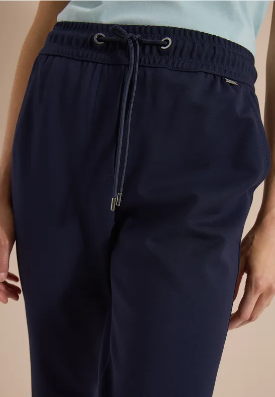 Nahaufnahme einer Person in dunklen, marineblauen Jogginghosen mit Tunnelzug und hohem Bund.