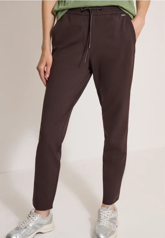 Dunkelbraune Damen-Hose mit elastischem Bund und Kordelzug, kombiniert mit Sneakers.
