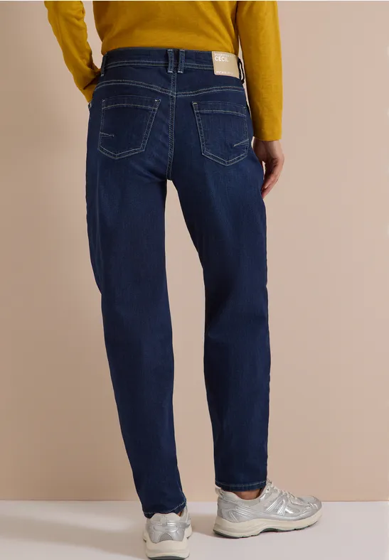 Rückansicht einer Person in blauen Jeans, gelbem Pullover und grauen Sneakern.