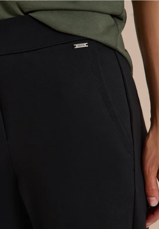 Pantalon noir souple avec poches latérales et petit label métallique discret à la taille.