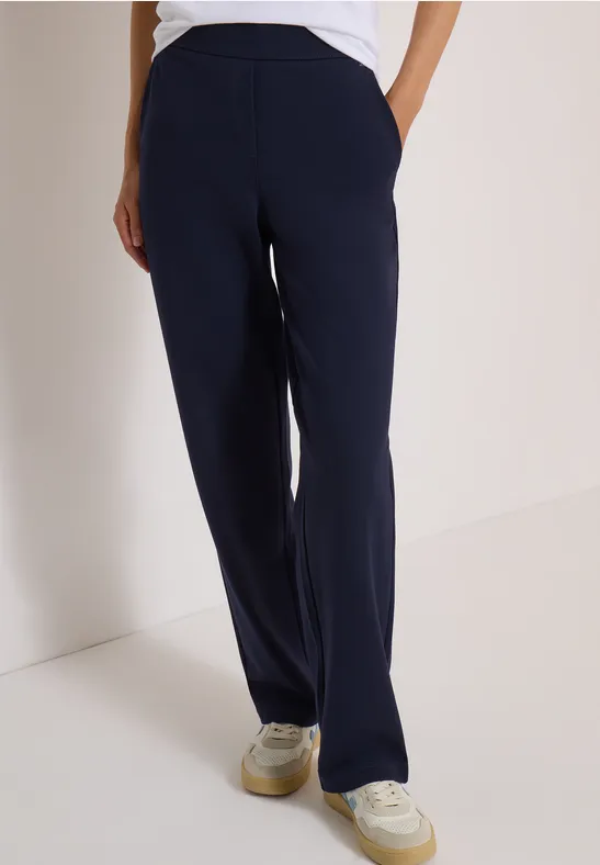Pantalon bleu marine droit avec poches latérales, porté avec des baskets blanches.
