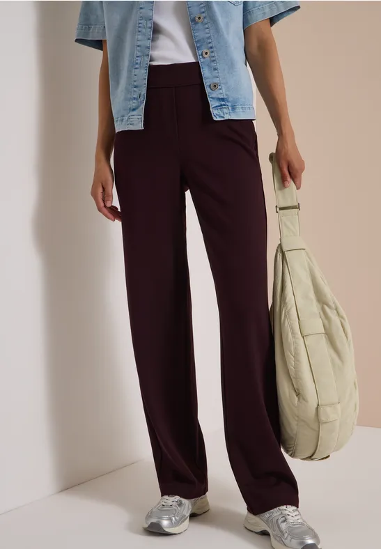Femme en pantalon ample prune, veste jean courte bleue, baskets argentées et grand sac beige.