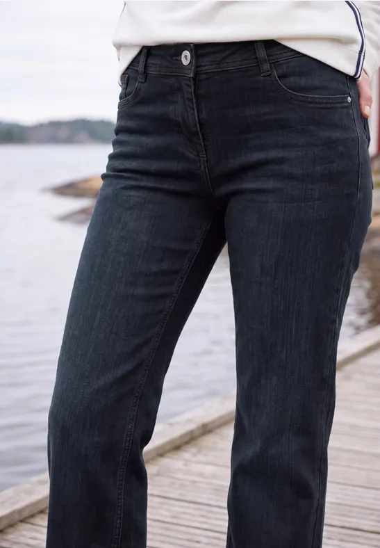 Dunkle Jeanshose auf einem Holzsteg am Wasser, Vorderansicht bis zur Taille.