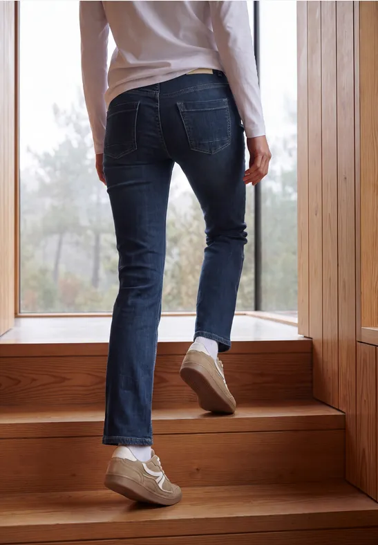 Menschenbeine in Jeans und Sneakers steigen eine hölzerne Treppe vor einem Fenster hoch.