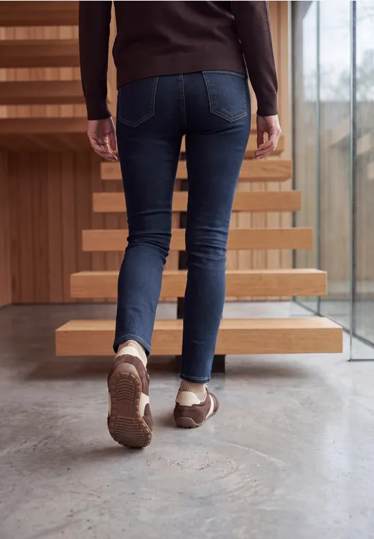 Eine Person in Jeans und braunen Schuhen steigt eine moderne Treppe hinauf.