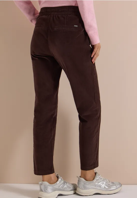 Frau trägt braune Cordhose und silberne Sneaker, Blick von hinten, kombiniert mit rosa Oberteil.