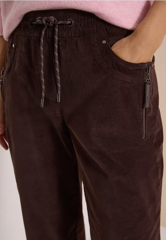 Nahaufnahme einer braunen Cordhose mit elastischem Bund, Kordelzug und Reißverschlusstaschen.