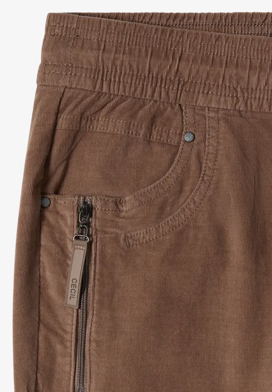 Braune Hose mit elastischem Bund, Reißverschlusstasche und sichtbaren Nieten im Vorderteil.